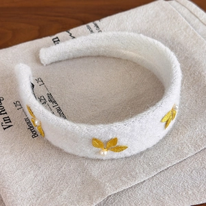 Close-up of white plush headband with gold metal leaf accents and delicate pearls