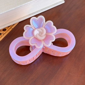 Détail d'une pince à cheveux fleur rose irisée avec rose sur fond de table en bois