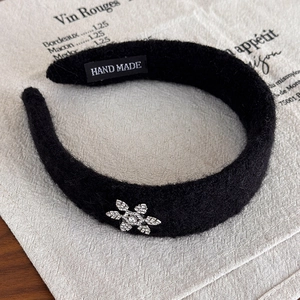 Détail d'un serre-tête en peluche noire avec fleur en strass et étiquette faite main