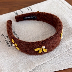 Detail of brown wool headband with golden metal leaves and white pearls on vintage fabric