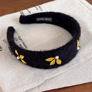Detail of black wool headband featuring golden leaf embroidery and white pearls