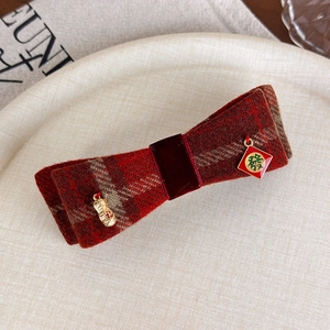 Dettaglio del fermaglio a fiocco in tweed rosso con ciondoli portafortuna dorati