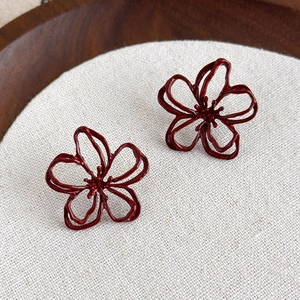 Detailed close-up of dark burgundy hollow flower earrings on rustic linen background