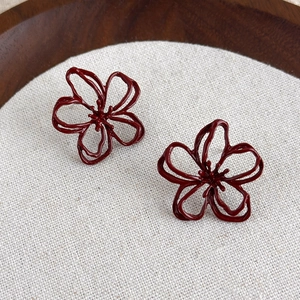 Retro hollow flower stud earrings in wine red finish on textured beige fabric