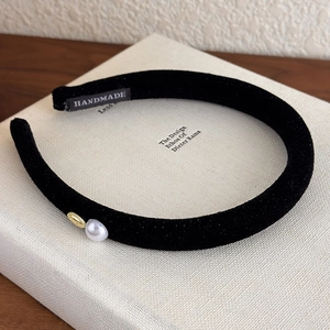 Close-up of black velvet headband with a white pearl, gold ring and handmade label
