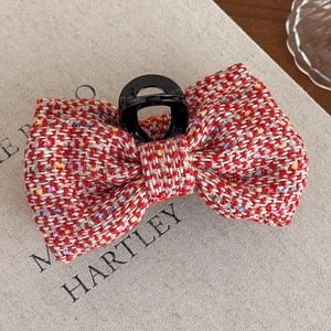 Detailed view of a red tweed bow hair claw clip placed on a textured fabric book