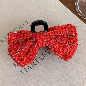 Detail of red tweed bow hair claw clip with shimmering threads on a beige background