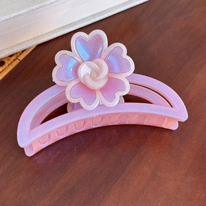 Détail de la pince à cheveux fleur rose irisée avec motif rose sur table en bois
