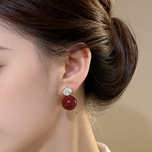 Boucles d'oreilles dorées avec zircon scintillant et perles rouges sur mannequin