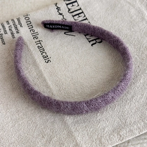 Detailansicht des flauschigen lila Stirnbandes mit Handmade-Label auf rustikalem Leinenhintergrund