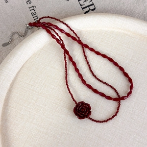 Detailed close-up of vintage red beaded necklace with rose pendant on rustic tray