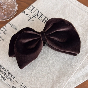 Detailed macro view of dark coffee velvet bow hair clip on a vintage linen fabric background