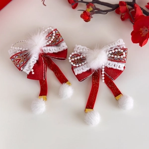 Détail d'une pince à cheveux avec nœud en satin rouge, pompon blanc et pampilles dorées