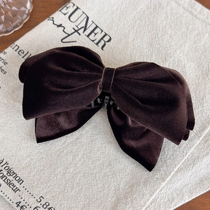 Detail view of large dark brown velvet bow banana clip on decorative beige linen fabric
