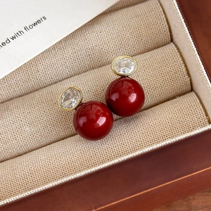 Gros plan de boucles d'oreilles perles rouges avec socle doré et pierre de zircon