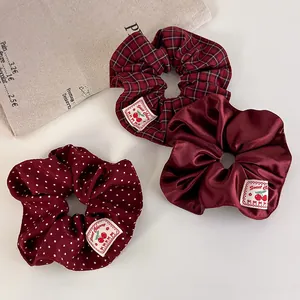 Three-piece set of deep red scrunchies featuring plaid, polka dots, and cherry woven labels