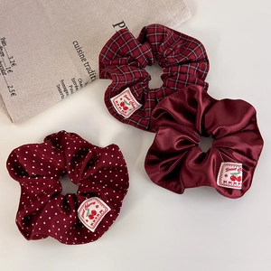 Close-up of burgundy scrunchie set featuring plaid, satin, and polka dot textile patterns