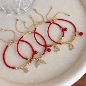Dettaglio di braccialetti rossi intrecciati con ciondoli d'oro e coulisse regolabile