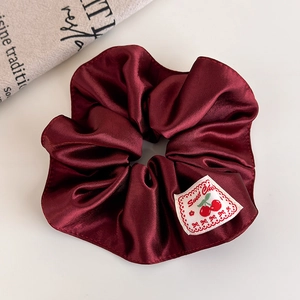 Detailed shot of burgundy satin scrunchie featuring a sweet cherry fabric label