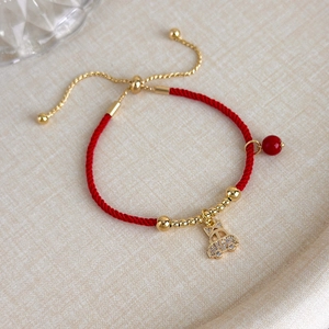 Dettaglio del bracciale in corda rossa con ciondolo auto dorato e pavé di zirconi