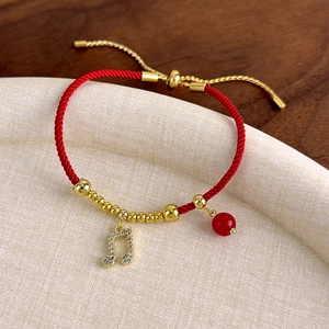 Dettaglio del bracciale rosso intrecciato con perle dorate, ciondolo a nota e chiusura