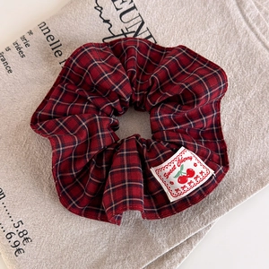 Detail of red plaid fabric scrunchie with sweet cherry label on vintage linen background