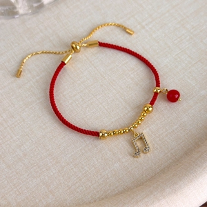 Dettaglio del bracciale cordino rosso intrecciato con perle dorate e ciondolo nota