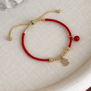 Dettaglio del bracciale rosso intrecciato con perle dorate e ciondolo segno del dollaro