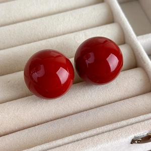 Detail view of glossy red spherical pearl earrings set in a cream jewelry box