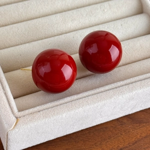 Detailed close-up of glossy red round pearl earrings in a beige velvet jewelry gift box