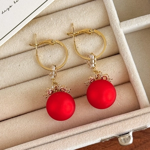 Detail of gold hoop earrings with large matte red pearls and sparkling zircon accents