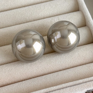 Close-up of metallic silver mirror sphere earrings displayed on beige velvet jewelry box tray