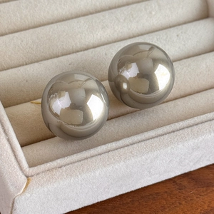 Close-up of 25mm large pearl stud earrings in metallic grey on beige velvet display