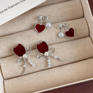 Elegant red heart and tulip bow earrings set with pearls on a beige jewelry display tray