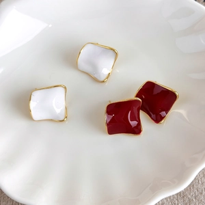 Close-up of geometric square stud earrings in red and white enamel with wavy gold borders