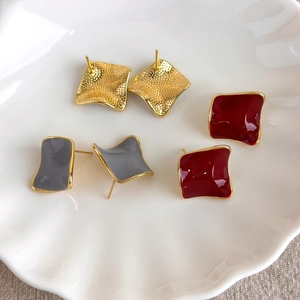 Detailed view of geometric square stud earrings with red and gray enamel on ceramic plate