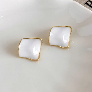 Macro shot of gold square stud earrings with white wavy enamel surface and minimalist design