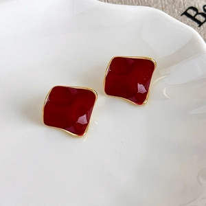 Close-up of square wine red enamel earrings with gold alloy edges on a white tray