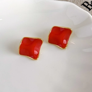 Detail of square red enamel earrings with golden edges on a white ceramic plate