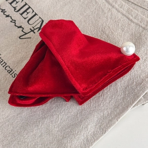 Macro shot of red velvet bow hair clip with a lustrous white pearl on linen fabric