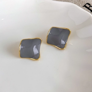 Macro shot of square dark gray enamel stud earrings with gold-toned metal borders