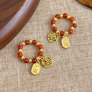 Bagues ethniques perlées rouge et or avec pendentifs Fu sur fond de lin beige clair