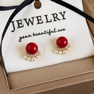 Macro detail of red bead and pearl fan stud earrings on a jewelry display card