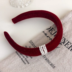 Close-up of red velvet headband with white pearls on a textured linen background