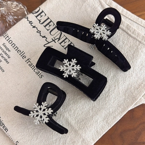 Elegant black velvet hair claws with rhinestone snowflake designs on linen background