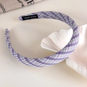 Detail of purple plaid fabric headband featuring a woven HAND MADE inner label on a white table