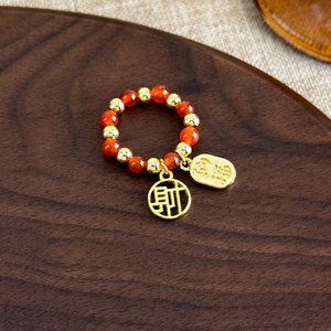 Détail de bague en perles d'agate rouge avec pendentifs Fu et Cai dorés sur bois