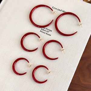Detailed view of three sizes of red enamel C-shaped hoop earrings with gold posts