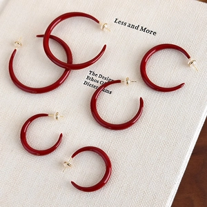 Three pairs of elegant red enamel C-shaped earrings in different sizes on a white book