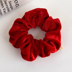 Detail of red corduroy scrunchie with soft ribbed texture and a gold metal charm